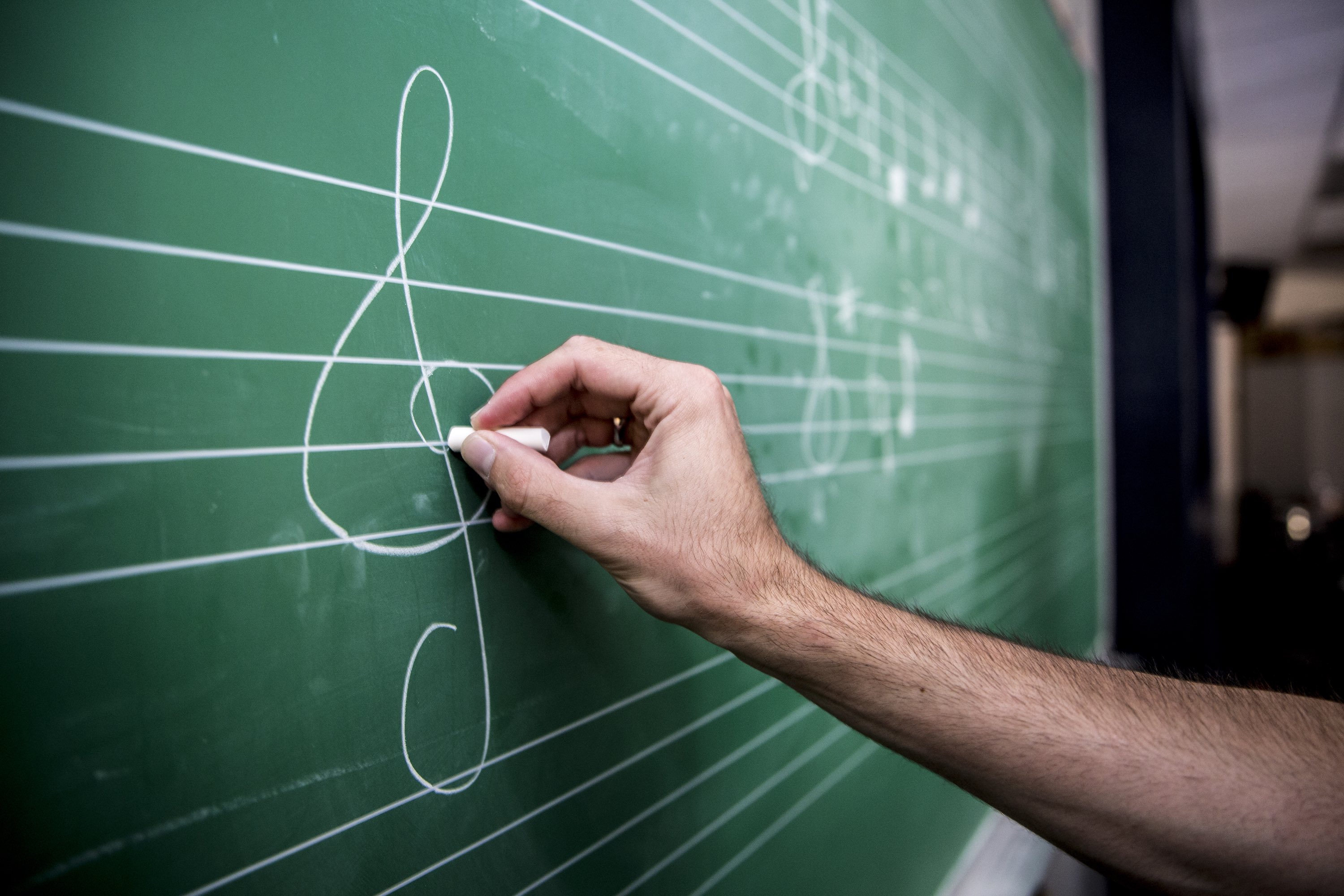 hand drawing the G clef on a chalk board