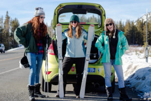 Three girls in front of a car with skiis