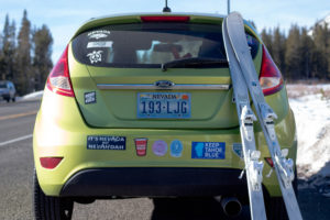 Green Car with tons of stickers and skiis leaning against the back