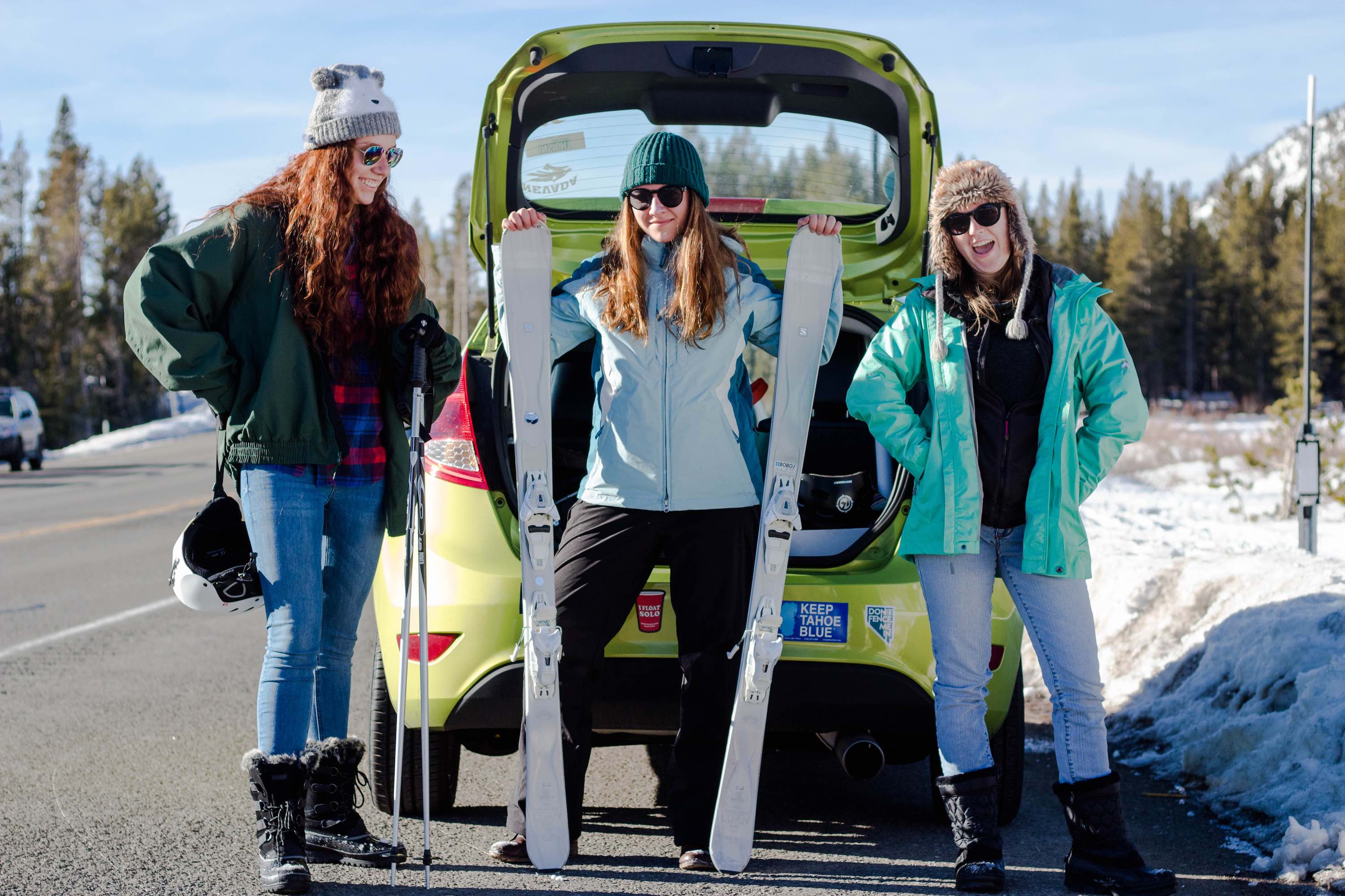three women behind a car with skis in hand