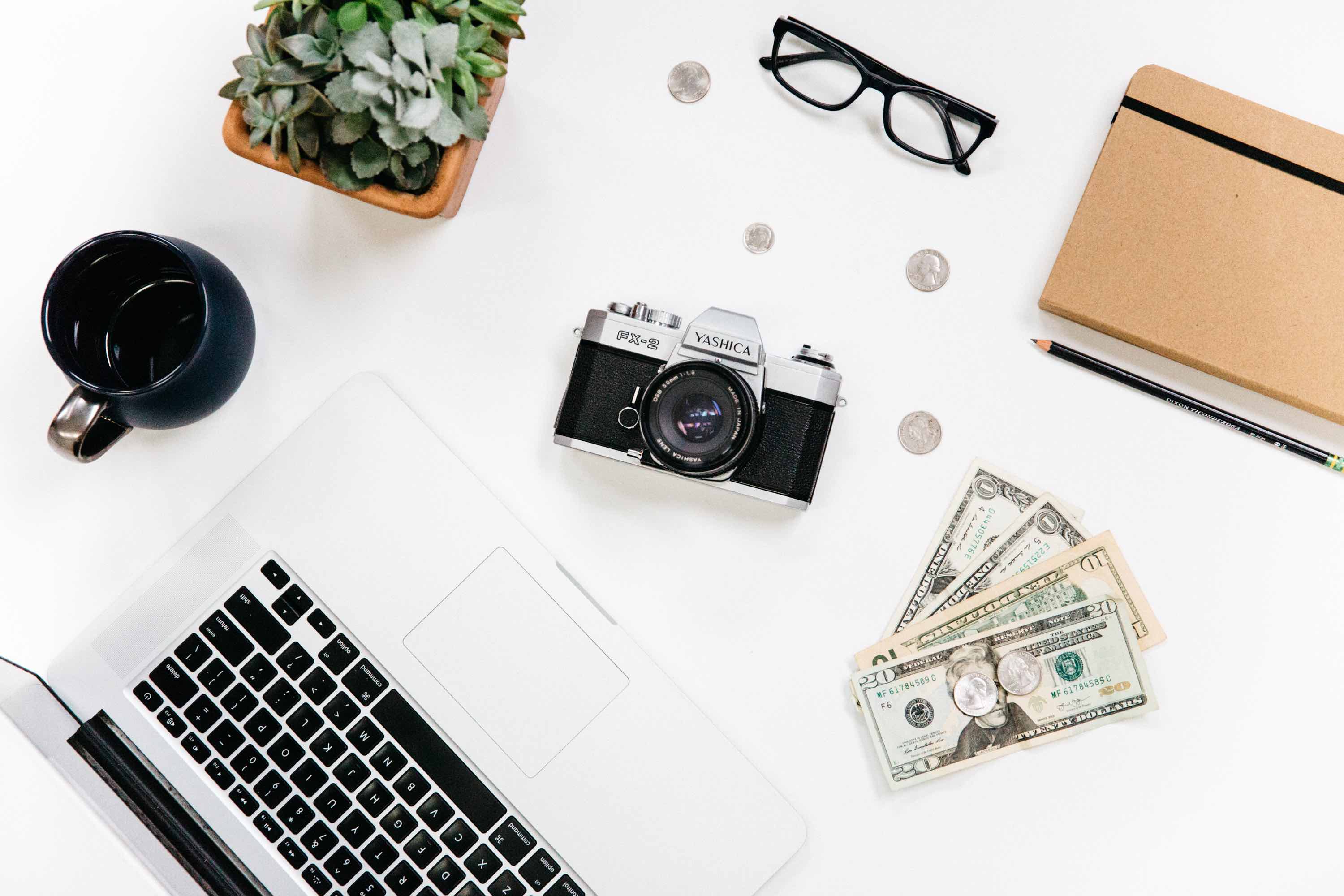 a Camera, glasses, coins, laptop, succulent, coffee mug, and notebook on a white background