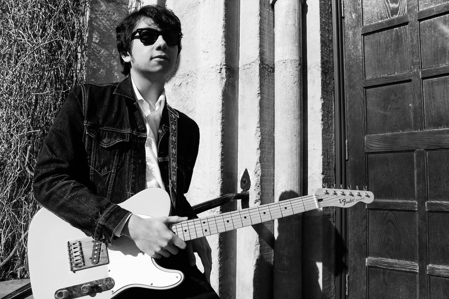 hipster leaning against railing with a guitar in black and white