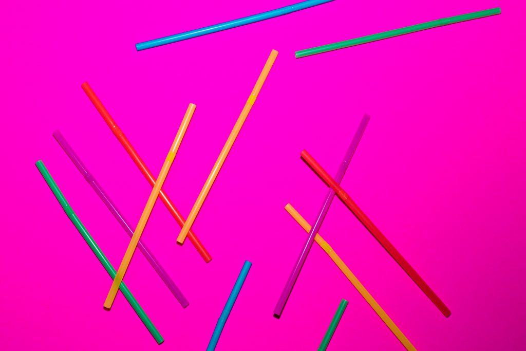 a bunch of plastic colorful straws on a pink background
