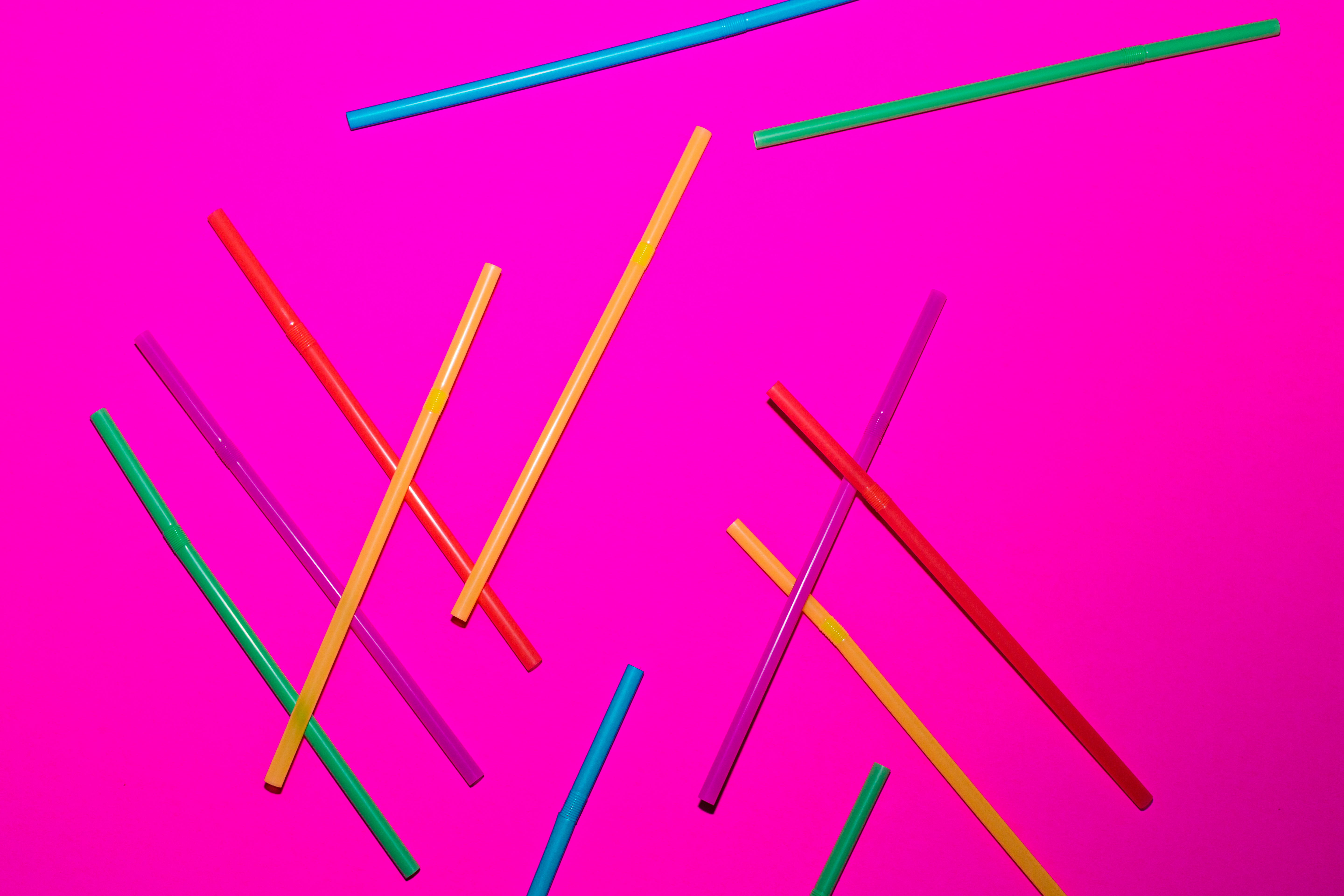 a bunch of plastic colorful straws on a pink background